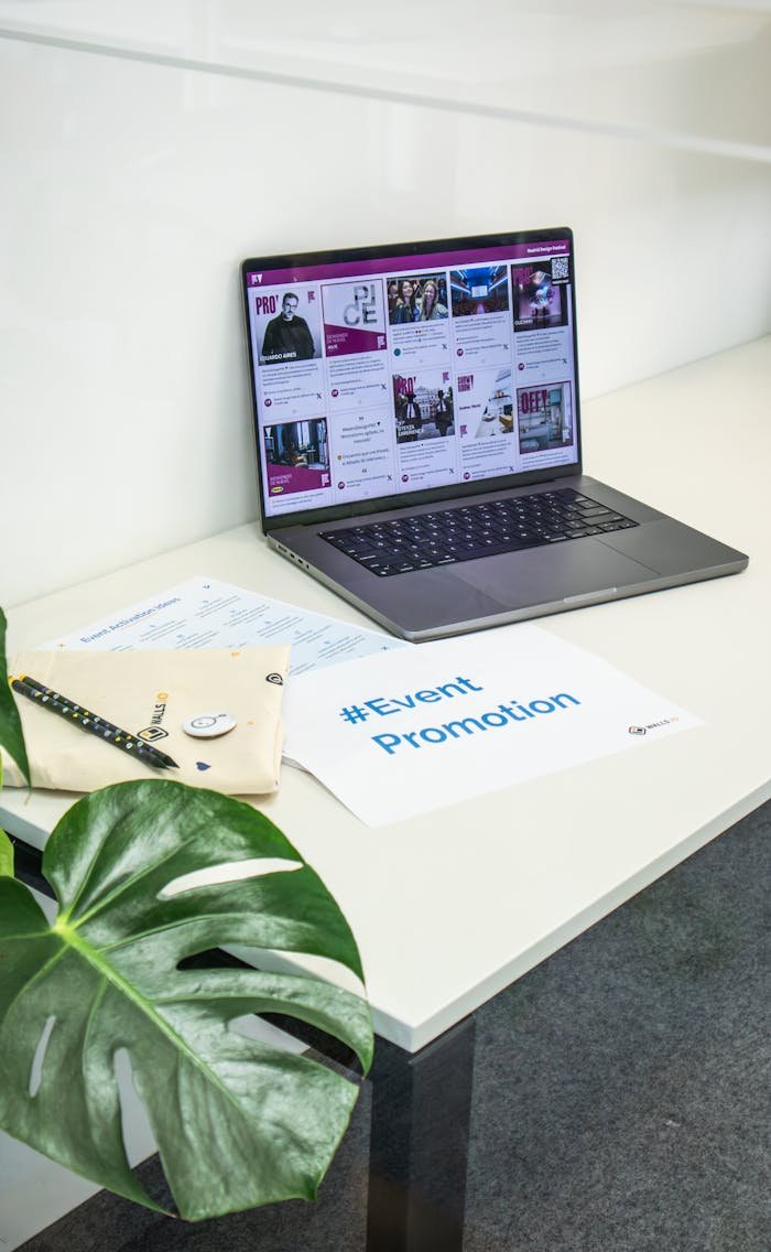 Home Clean office space with a laptop displaying social media, papers, and a plant for event promotion.